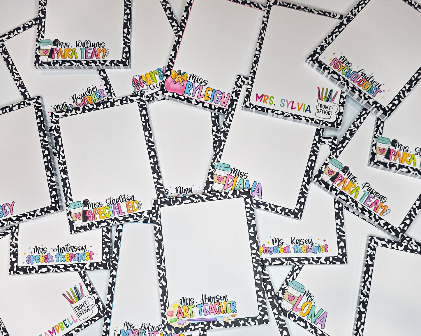 a collection of personalized A2 sized notepads, each with a unique name and title. The nameplates are arranged in a grid-like pattern, with each one featuring a different name and title. The names and titles are written in a variety of fonts and colors, creating a visually appealing and diverse display. These are teacher themed notepads with vibrant colors, most being in neon or bright rainbow patterns.